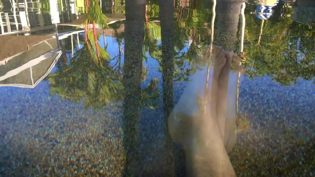 Mans feet relax in a resort pool. Travel vacation concept.