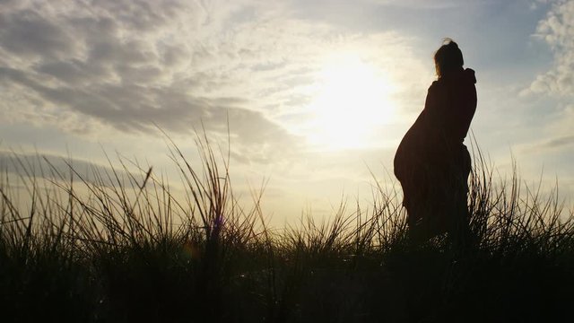 4K Female silhouette in a blanket stands and looks to the view, in slow motion