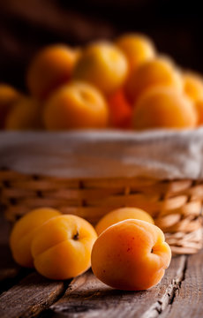 Apricots group in basket and on old rustic wooden table and dark background, selective focus