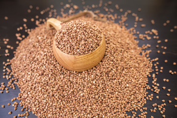buckwheat groats in the wooden mug and scattered on black table
