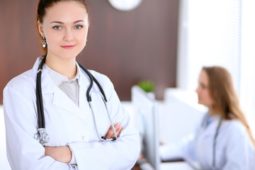 Beautiful young smiling female doctor standing in a hospital with her colleague in the background