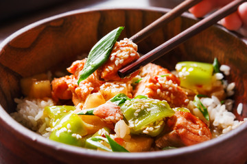 Asian cuisine - rice in sauce with stir fried vegetables, pineapple and salmon. Wooden bowl with chopsticks. 