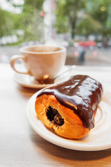 Tasty bun with chocolate icing and poppy filling. White mug with hot coffee on background.