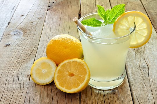 Glass of cold lemonade with lemon slices and mint on a rustic wood background