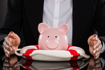Businessperson Hand Protecting Piggybank With Lifebelt
