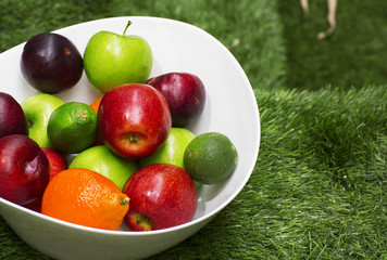 Green and red apples in a big white dish. The fruit bowl filled with assorted fresh fruits. 