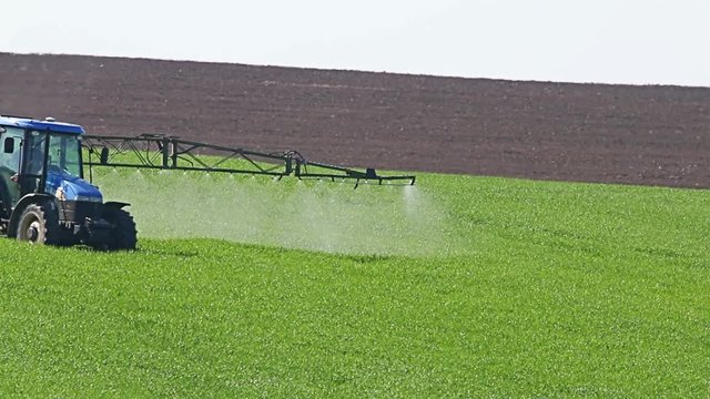 Tractor spraying field, rural landscape in countryside