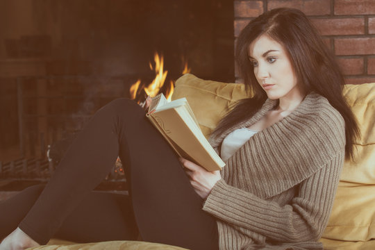 Young woman reading a book by fireplace
