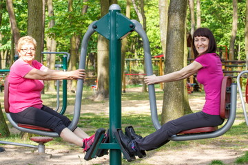 Fototapeta na wymiar Senior and young woman exercising lower body on outdoor gym, healthy lifestyle