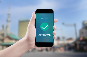 Hand holding mobile smart phone with project approved screen on city background