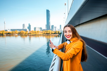 Young sport woman in yellow sweater using smart phone on the modern bridge with skyscrapers on the background.