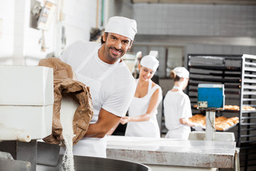 Smiling Male Baker Pouring Flour In Kneading Machine