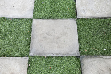 Square concrete block and artificial grass on the walkway or foo