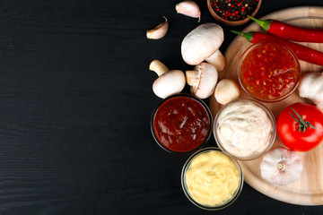 sauces in a glass bowl near the leaves are green with heads of garlic and with spices and vegetables on black wood background