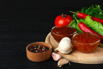 sauces in a glass bowl near the leaves are green with heads of garlic and with spices and vegetables on black wood background