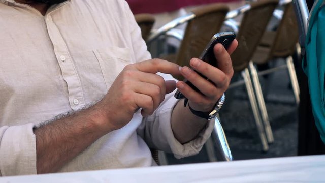 Male hands using smartphone in cafe in city
