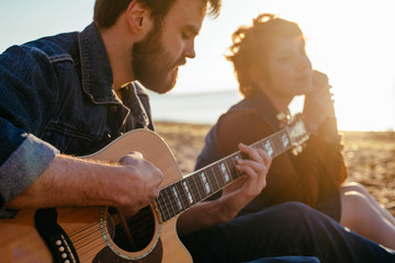 young caucasian couple playing guitar on beach at sunset