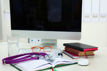 Stethoscope lying on a notebook computer in the background and books