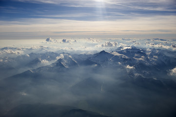 High altitude view of sunset over the mountains. Rays of light shine through the hazy atmosphere.
