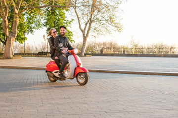 young beautiful couple riding scooter in city on sunny day
