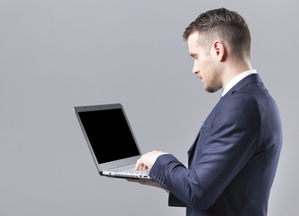 Young businessman using a laptop against grey background