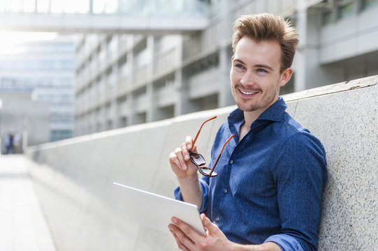 Portrait of young businessman with digital tablet leaning against wall