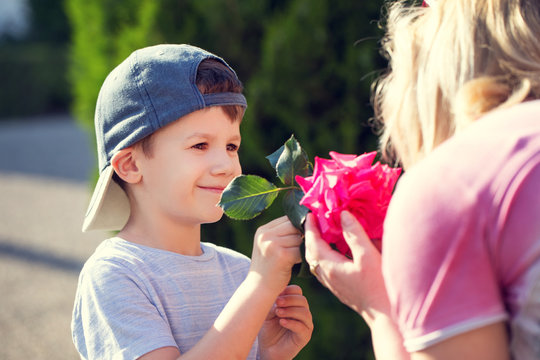 Little boy in cap give rose to mom