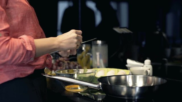 Woman hands breaking eggs on frying pan in the kitchen
