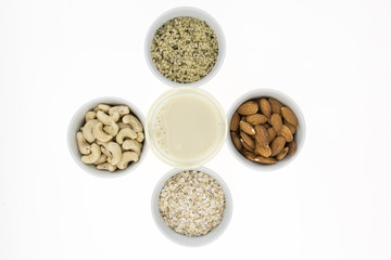 Glass of homemade plant based milk and bowls with ingredients, on white background