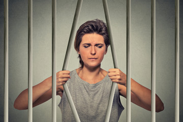 Stressed desperate sad woman bending bars of her prison cell