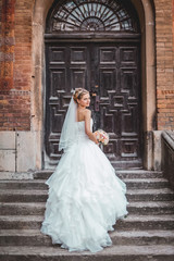 Fototapeta na wymiar Beautiful blond bride in white dress posing near old wooden door