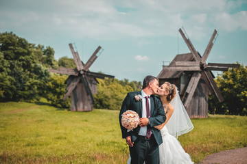 Newlyweds embracing near old wooden mill. Sunny day blue clouds