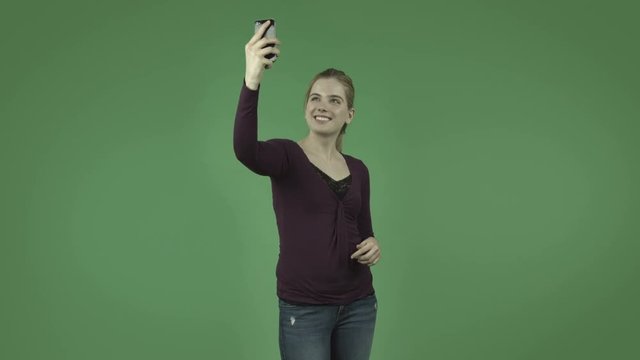 attractive casual caucasian girl isolated on green taking a selfie