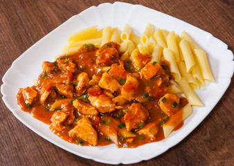 chicken breast in tomato sauce with penne pasta in a plate on wooden table