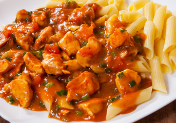 chicken breast in tomato sauce with penne pasta in a plate on wooden table