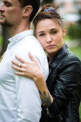 Beautiful young girl in a white dress and black leather jacket with tattoos hugging her boyfriend