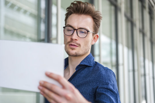 Portrait of young businessman with digital tablet in front of an office building