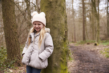 Young girl leaning against a tree by a path in a forest