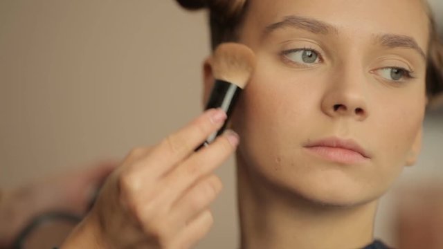 makeup artist applies powder to the face of a young girl
