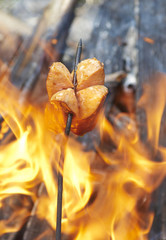 Sausage on a stick over the fire. Preparing sausages on camp fire