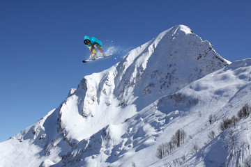 Naklejka na ściany i meble Snowboard rider jumping on winter mountains. Extreme snowboard freeride sport.