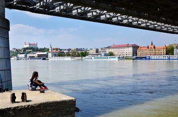 Young girl resting by the river in Bratislava unde old bridge - obrazy, fototapety, plakaty
