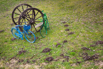 Rustic wooden wagon wheels with blue and green painted bicycles in a grassy field, long view