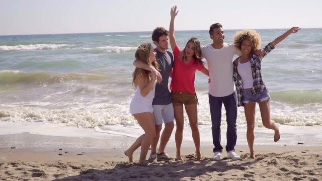 Five young attractive people posing and jumping on the sandy beach in the evening while laughing in slow motion.