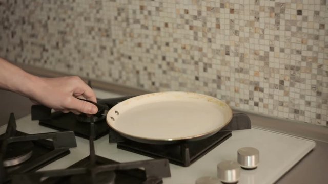 Cooking breakfast - man with smartphone in the kitchen to fry egg in a frying pan on  gas stove