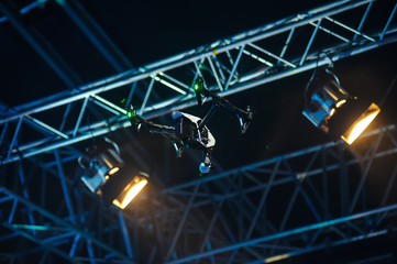 Flying drone above the stage/White quadrocopter drone with camera flies against stage constructions 