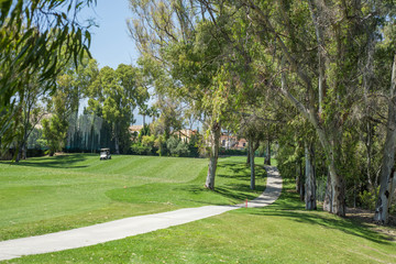 Pathway full of trees in golf course with golf car in the background.