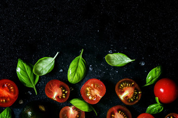 Red and black halves of tomatoes with green leaves of basil, foo
