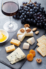 Assortment of cheese with honey, nuts and grape on a modern cutting board slate background.