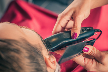 Female barber shaving a client's beard with trimmer in a barber shop. Close-up